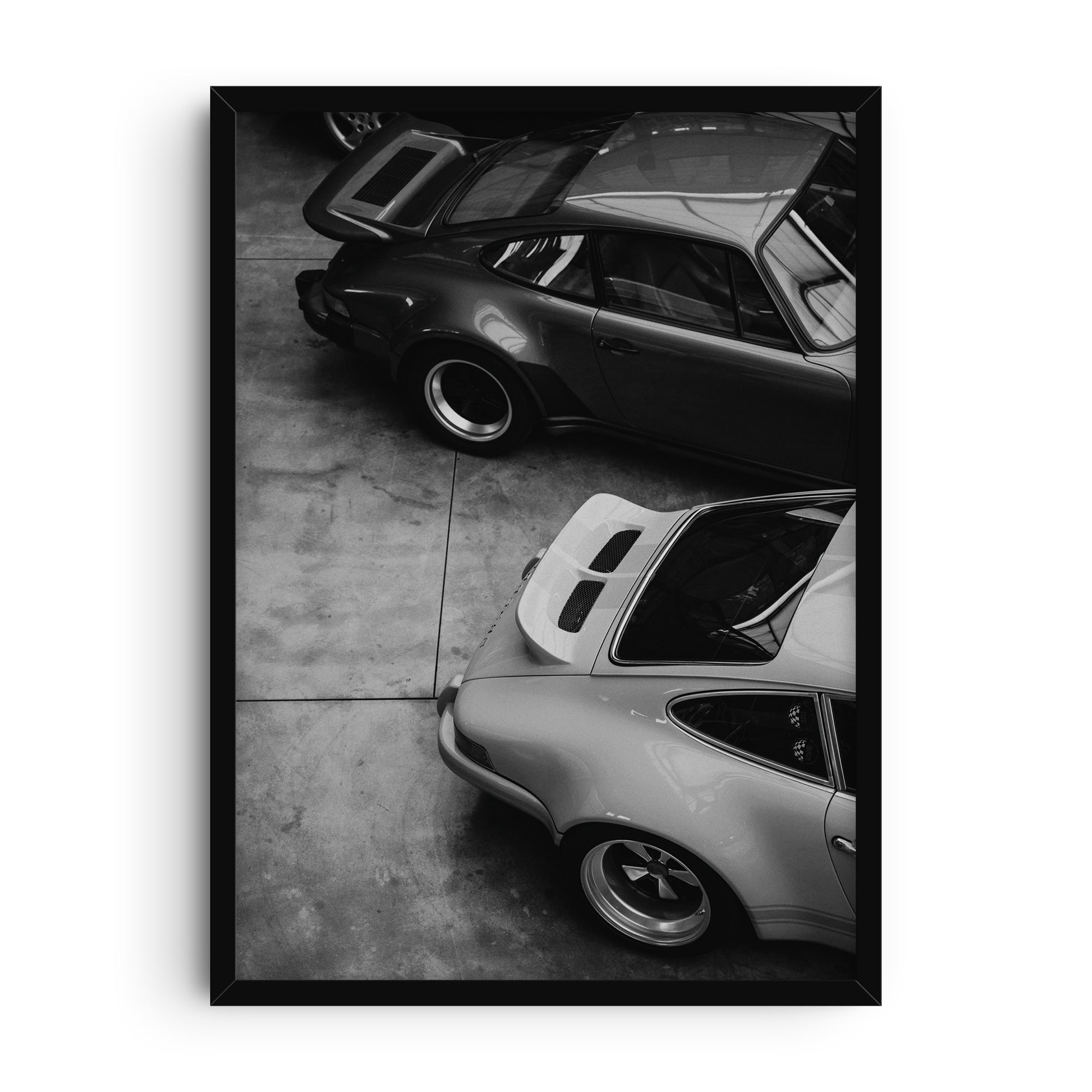 Black and white photographic art print showing two classic sports cars viewed from above, highlighting their curved bodywork, polished metal, and timeless automotive design.