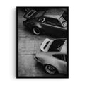 Black and white photographic art print showing two classic sports cars viewed from above, highlighting their curved bodywork, polished metal, and timeless automotive design.