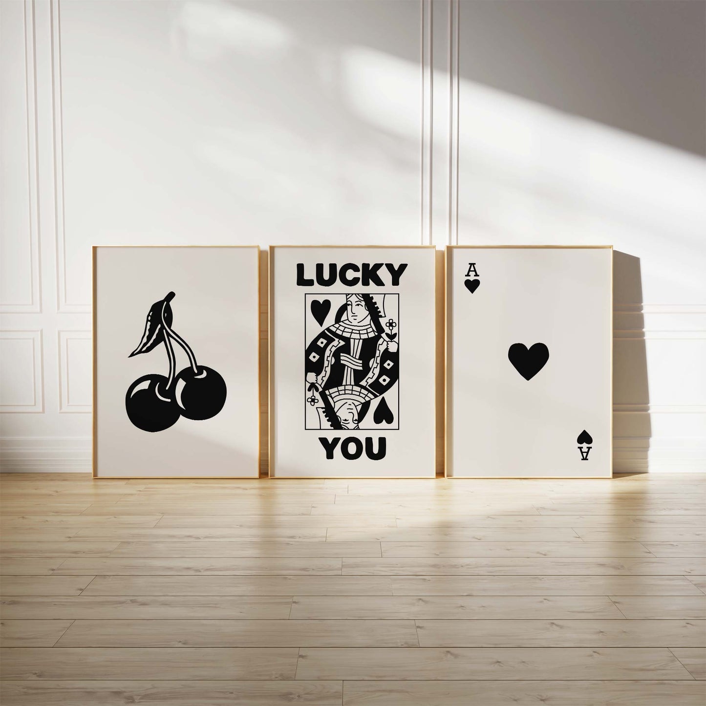 Black and white art print bundle with cherries, Queen of Hearts with "Lucky You," and Ace of Hearts designs in a modern interior setting.