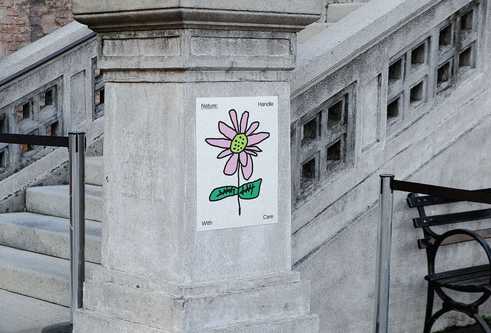 Minimalist flower illustration print with pink petals and green leaves, pasted on a concrete wall by a staircase in an urban setting.