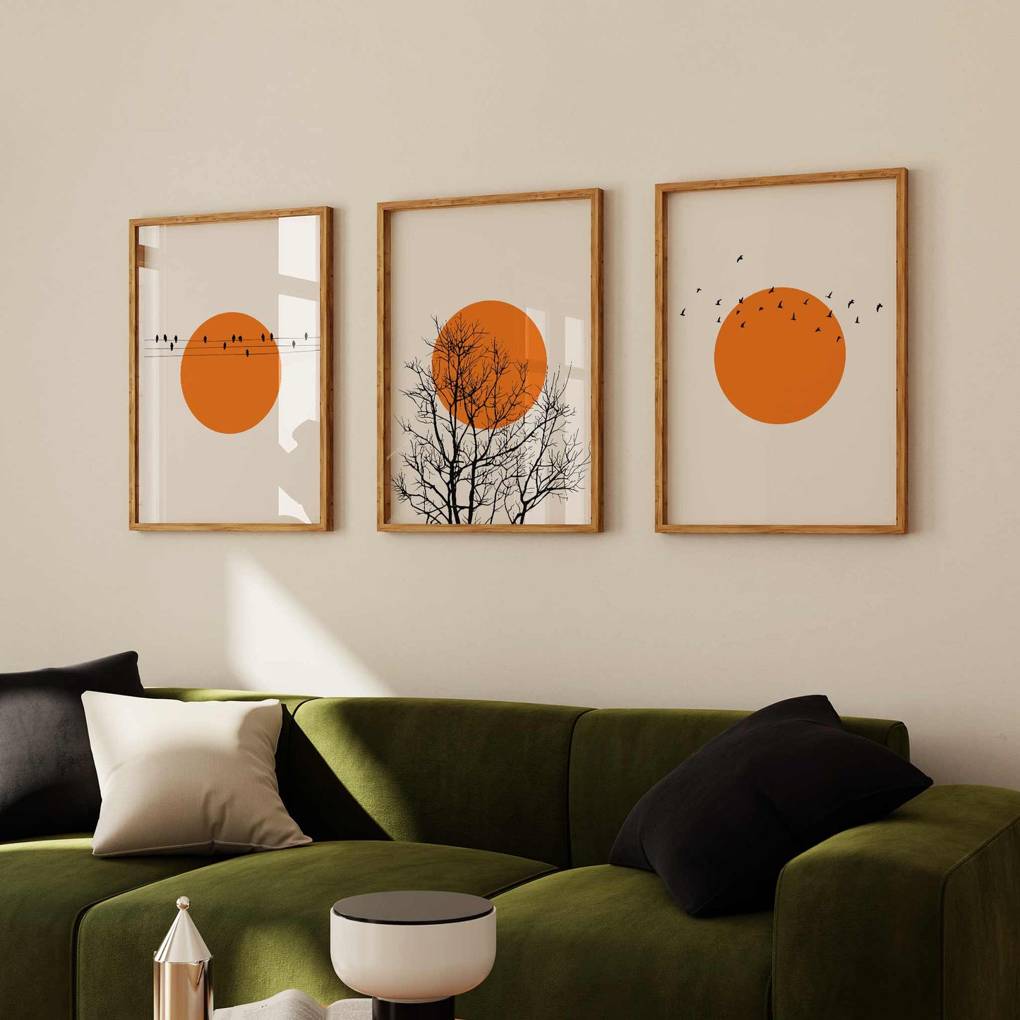 Framed minimalist sunset art print set featuring three orange sun designs with birds and trees, styled above a green sofa for a warm, nature-inspired decor setting.